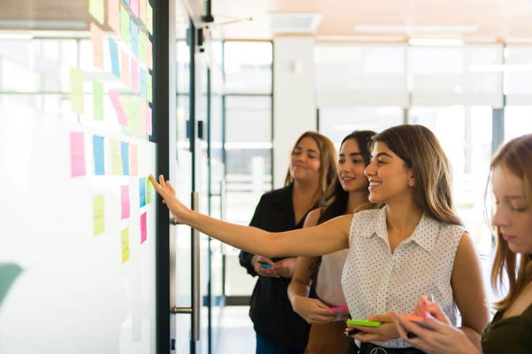 Women doing artificial intelligence brainstorming at whiteboard with sticky notes